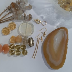 May include: Assortment of natural gemstone beads, including clear quartz, agate, and citrine, in various shapes and sizes. Also included are gold-toned earring findings, jump rings, and head pins.
