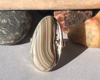 May include: A silver ring with a brown and white agate stone. The stone has a wavy pattern and is set in a silver band.