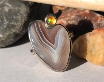 May include: A heart-shaped pendant with a white and brown agate stone set in silver. A small, round, yellow opal stone is set at the top of the pendant.