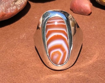 May include: A silver ring with a white and orange agate stone set in a bezel setting.