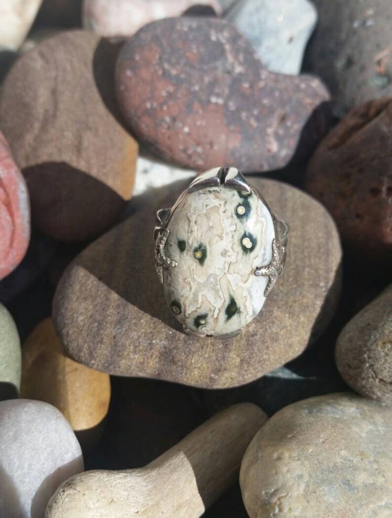 May include: A silver ring featuring a white and green stone set in a silver setting. The stone has a distinctive pattern of white and green.
