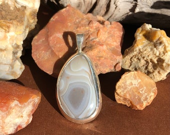 May include: A silver pendant featuring a white agate stone with brown and gray swirling patterns.