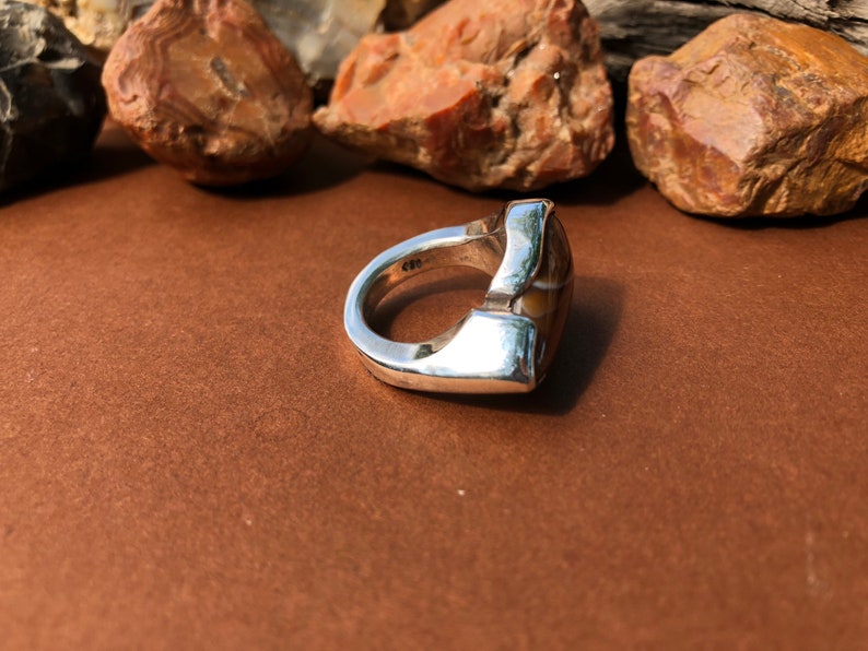 May include: A silver ring with a brown and white agate stone set in a geometric design.