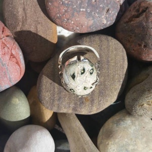 May include: A silver ring featuring a white and green stone set in a claw setting. The stone has a distinctive pattern of black and white markings.