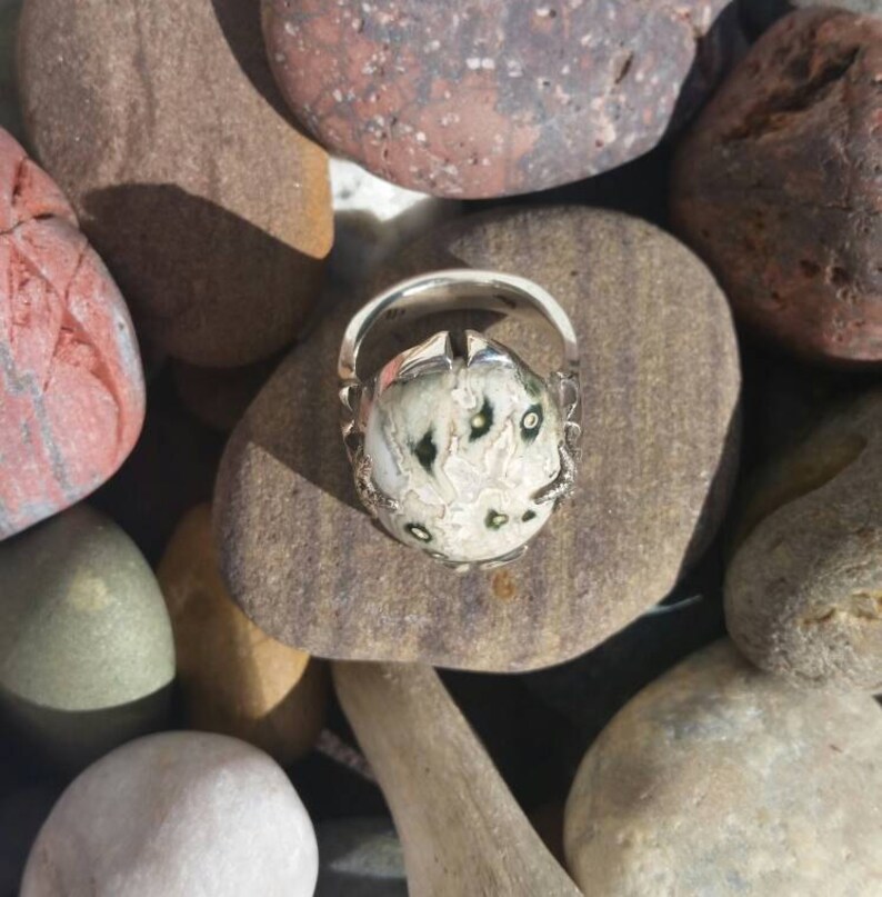 May include: A silver ring featuring a white and green stone set in a claw setting. The stone has a distinctive pattern of black and white markings.
