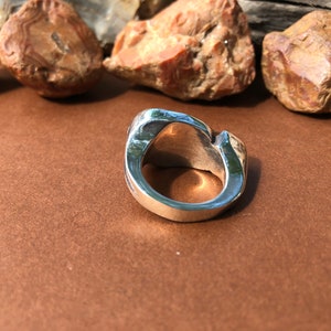 May include: A silver ring with a unique, organic, and abstract design. The ring is made of smooth, polished metal and has a wide band.