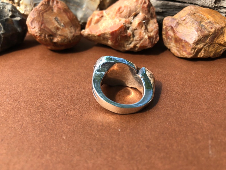 May include: A silver ring with a unique, organic, and abstract design. The ring is made of smooth, polished metal and has a wide band.