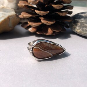 May include: A silver ring with a brown agate stone set in a teardrop shape.