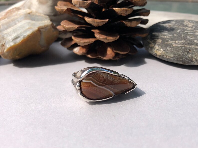 May include: A silver ring with a brown agate stone set in a teardrop shape.