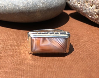 May include: A silver ring with a rectangular agate stone set in the center. The agate has a brown and white striped pattern.