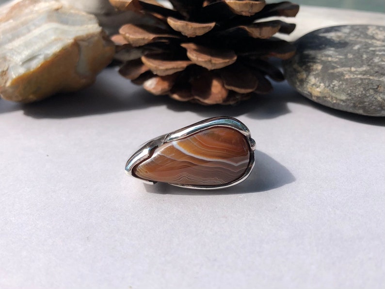 May include: A silver ring with a brown agate stone set in the center. The stone has a swirling pattern of brown and white.
