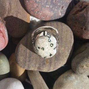 May include: A silver ring featuring a white and green stone set in a silver setting. The ring is surrounded by smaller stones.