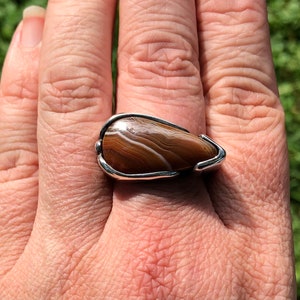 May include: A silver ring with a brown and white agate stone set in a teardrop shape.