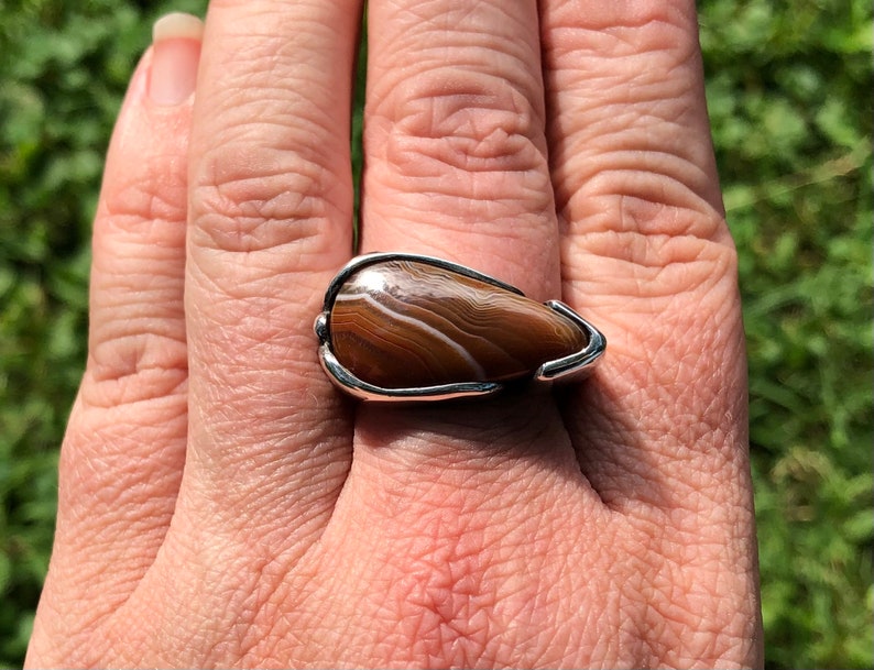 May include: A silver ring with a brown and white agate stone set in a teardrop shape.