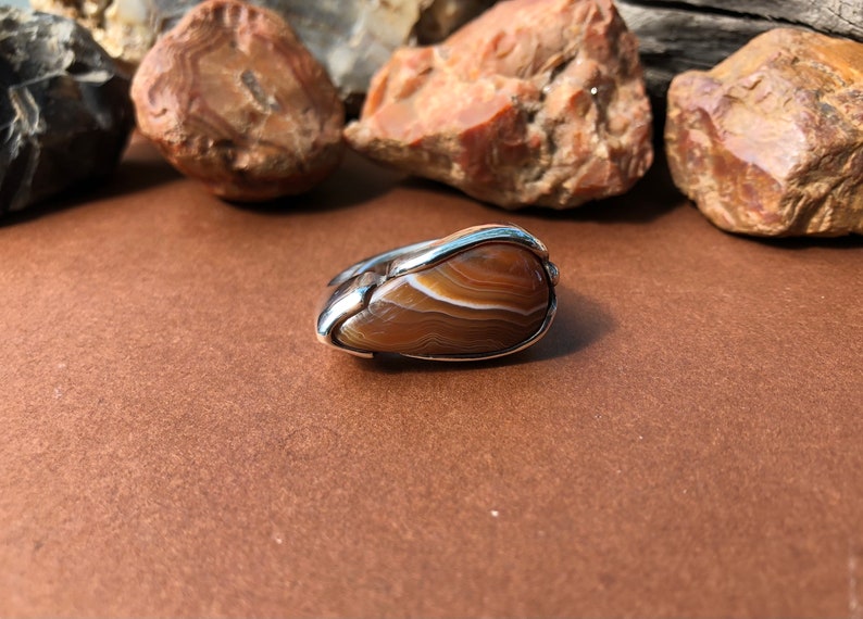 May include: A silver ring with a brown agate stone set in the center. The stone has a swirling pattern of brown and white.