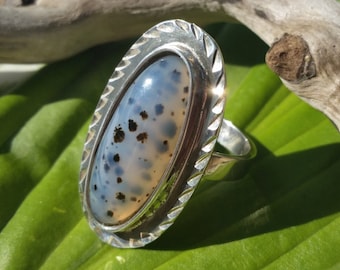 May include: A silver ring with a white and black oval gemstone set in a silver bezel. The ring has a textured band.