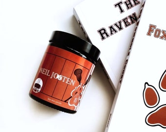 May include: A brown soy wax candle with the text "Neil Josten" and a lacrosse stick graphic. The candle is labeled "Soy Wax Candle".