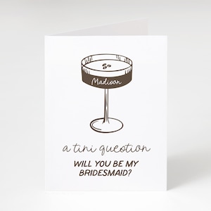 Pode incluir: Um cart&atilde;o castanho com uma ilustra&ccedil;&atilde;o desenhada &agrave; m&atilde;o de um copo de martini com a palavra "Madioon" nele. O texto "a tiny question" e "Will you be my bridesmaid?" est&aacute; escrito abaixo do copo.