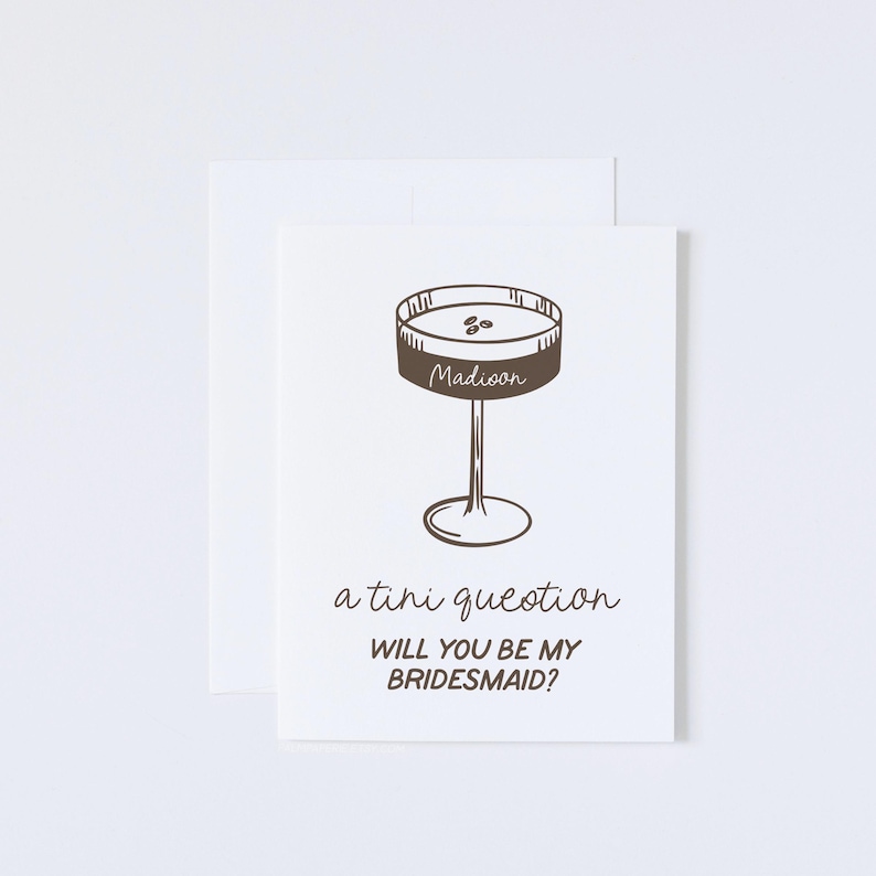 Pode incluir: Um cart&atilde;o branco com uma ilustra&ccedil;&atilde;o marrom de uma ta&ccedil;a de martini com a palavra "Madioon" escrita nela. O texto "a tini question" e "Will you be my bridesmaid?" est&aacute; escrito abaixo da ilustra&ccedil;&atilde;o.