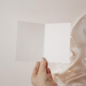 Pode incluir: Um cart&atilde;o branco em branco segurado em uma m&atilde;o contra um fundo marrom claro.