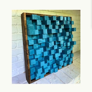 May include: A teal blue wooden wall art piece made of stacked blocks. The blocks are arranged in a random pattern and create a textured surface. The wall art is framed in a dark brown wood frame.