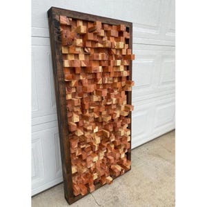 May include: A large rectangular wooden sound panel with a dark brown frame. The panel is made up of many small, rectangular blocks of wood in various shades of brown and orange.