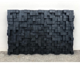 Könnte beinhalten: Ein schwarzes Wandkunststück aus Holz, das aus vielen kleinen quadratischen Blöcken besteht. Die Blöcke sind in einem zufälligen Muster angeordnet, wodurch ein strukturiertes und abstraktes Design entsteht.