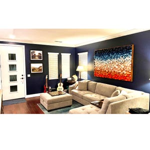 May include: A living room with a sectional sofa, a coffee table, and a large abstract wall art piece made of wood blocks in shades of blue, white, and red. The wall art is mounted on a dark blue wall.
