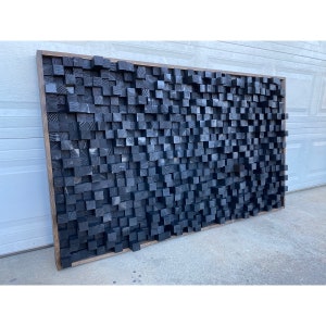 May include: A large black sound-absorbing panel made of wood blocks. The panel is mounted on a wall and has a rustic, modern look.
