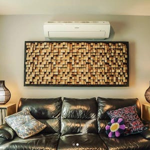 May include: A black leather sofa with three cushions, two lamps with black wicker shades, and a large wooden sound panel on the wall behind the sofa. The room has a white ceiling and light grey walls.