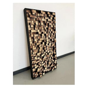 May include: A rectangular wall panel made of wood blocks in various shades of brown. The blocks are arranged in a random pattern, creating a textured surface. The panel is framed in black.