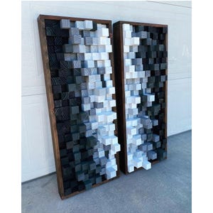 May include: Two black framed wall panels with a 3D design of stacked wooden blocks in shades of gray and black. The panels are arranged side-by-side.