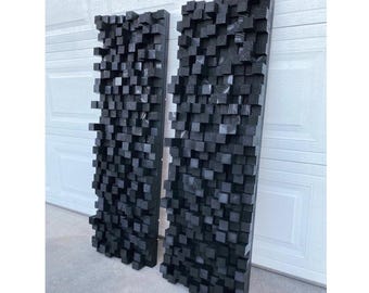 May include: Two black acoustic panels made of wood blocks, arranged vertically on a white wall. The panels are made of many small, square blocks of wood, creating a textured surface.