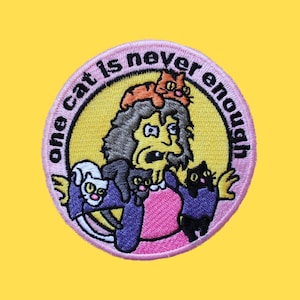 Puede incluir: Parche bordado rosa y amarillo con una mujer de dibujos animados sosteniendo varios gatos. El texto en el parche dice "one cat is never enough".