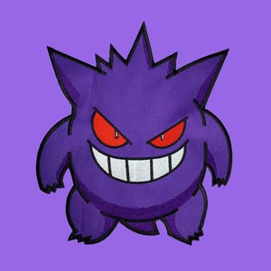Op de afbeelding: Geborduurd paars Gengar-ontwerp met rode ogen en een brede witte grijns op een paarse achtergrond. Het stripfiguur heeft stekelige oren en een rond lichaam. Het ontwerp is waarschijnlijk voor een patch of applicatie.