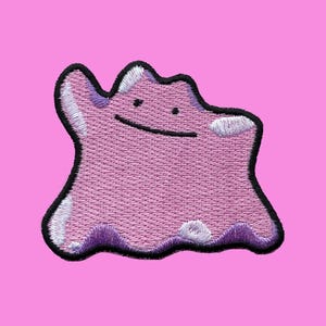 以下が含まれることがあります： 黒い縁取りと笑顔の顔を持つピンク色のDittoキャラクターの刺繍パッチ。パッチには白と紫のアクセントがあり、ピンク色の背景に配置されています。衣類やアクセサリーに追加するのに最適です。