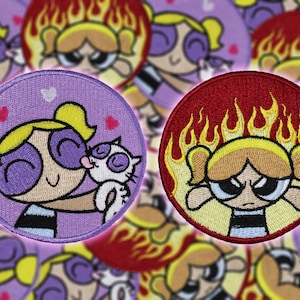 Könnte beinhalten: Zwei gestickte Bügelbilder mit einer Comicfigur mit blonden Haaren und blauen Augen. Ein Patch hat einen lila Hintergrund mit Herzen und die Figur hält ein weißes Kätzchen. Der andere Patch hat einen roten Hintergrund mit Flammen und die Figur hat einen wütenden Ausdruck.