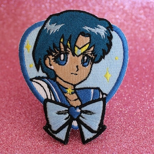 Puede incluir: Un parche bordado para planchar que presenta un personaje de anime de pelo azul con un uniforme de marinero azul y un lazo azul. El personaje tiene una estrella amarilla en la frente y está rodeado de un fondo azul claro con estrellas amarillas.