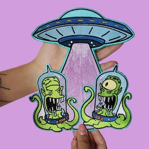 Puede incluir: Dos extraterrestres verdes con grandes bocas y ojos están siendo abducidos por un OVNI azul y blanco. Los extraterrestres están en tubos de vidrio y tienen tentáculos.