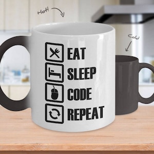 Peut inclure: Une tasse en céramique blanche avec une poignée noire qui change de couleur lorsqu'elle est chaude. La tasse a un motif noir avec le texte "Manger, Dormir, Coder, Répéter" dans un format de liste.