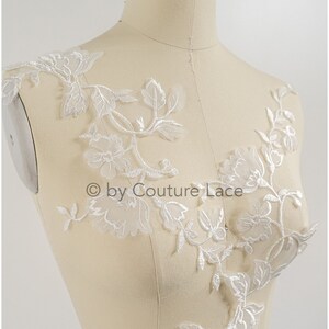 May include: White floral lace applique with delicate flowers and leaves. This lace applique is perfect for adding a touch of elegance to any garment or project.