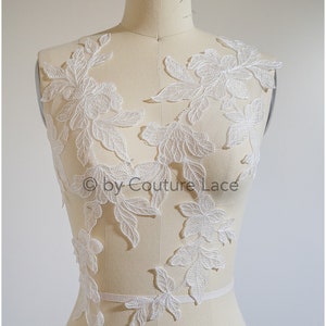 May include: White floral lace applique featuring delicate leaves and flowers. This lace applique is ideal for adding a touch of elegance to any garment.