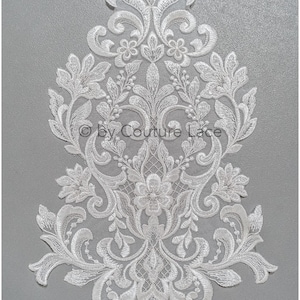 May include: White lace applique with a floral design. The lace is delicate and intricate, with a variety of floral motifs. The applique is perfect for adding a touch of elegance to any project.