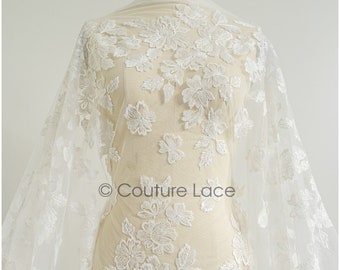 Puede incluir: Tela de encaje floral blanco drapeada sobre un maniquí. El encaje presenta un bordado floral en relieve detallado. El logotipo de Couture Lace es visible en la tela. Ideal para vestidos de novia o de fiesta.