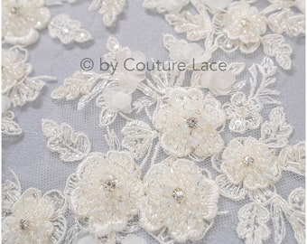 May include: Close-up of ivory lace fabric with floral and leaf designs. The lace is embellished with beads and small crystals, creating a delicate and textured appearance. The text "© by Couture Lace" is visible.