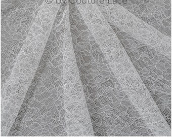 May include: White lace fabric with a delicate floral pattern. The fabric is sheer and has a soft, flowing texture.