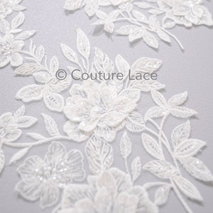 May include: White floral lace fabric with beaded embellishments. The lace features delicate flowers and leaves, with a subtle shimmer from the beads.  © Couture Lace