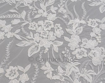 Puede incluir: Tela de encaje floral blanca con un delicado patrón de flores y hojas. El encaje tiene un brillo sutil y es perfecto para agregar un toque de elegancia a cualquier proyecto.
