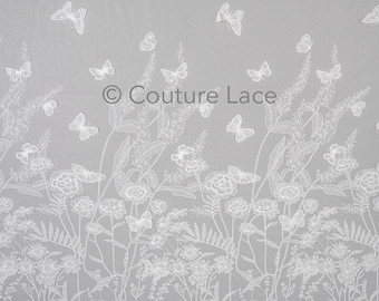 May include: White lace fabric with a delicate floral and butterfly design. The fabric has a subtle dotted texture and features a repeating pattern of flowers, leaves, and butterflies.