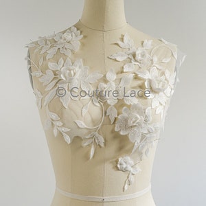 Może przedstawiać: Biała aplikacja z koronki kwiatowej z delikatnymi kwiatami i liśćmi. Koronka jest na przezroczystej siatce i idealnie nadaje się do dodania odrobiny elegancji do każdego ubrania.